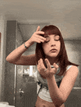 a woman with red hair is applying makeup to her face in a bathroom