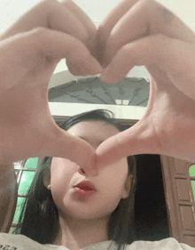 a girl making a heart shape with her hands in front of her face