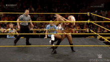 two women are wrestling in a wrestling ring while a referee looks on