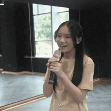 a girl in a tan shirt is holding a microphone in front of a mirror