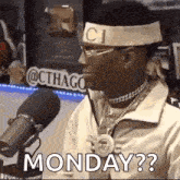 a man wearing a headband and glasses is sitting in front of a microphone and saying monday ?