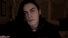 a young man with long black hair is sitting in a dark room .