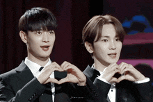 two men in tuxedos are making a heart shape with their hands