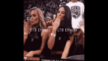 two women are dancing in the stands at a basketball game while a man in a sls shirt watches .
