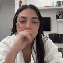 a woman in a white robe with her hand on her face