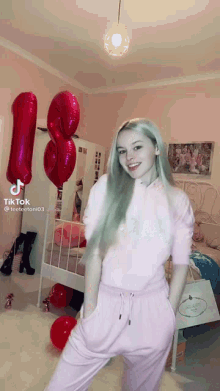 a girl with green hair is standing in a room with balloons and a bed .