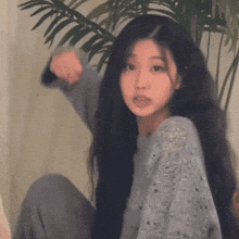 a girl with long black hair is sitting in front of a plant