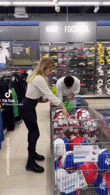 a man and a woman are looking at soccer balls in a store under a sign that says nike football