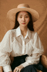 a woman wearing a straw hat and a white shirt is sitting in a chair