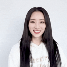 a woman with long black hair is smiling and wearing a white hoodie that says merry