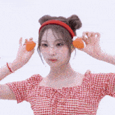 a girl wearing a red headband and a red plaid shirt is holding two orange balls in front of her ears