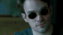 a close up of a man wearing round sunglasses looking at the camera .