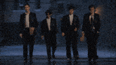 four men in suits are walking down a street
