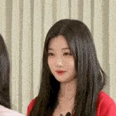 a woman with long black hair wearing a red shirt looks at the camera