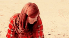 a woman with long red hair is wearing a red plaid shirt and holding her hair .