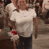 a woman wearing a white shirt that says karl lagerfeld is holding a bouquet of flowers