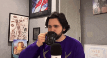 a man in a purple sweater is drinking from a mug that says thr