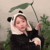 a girl wearing a panda hat holds a plant