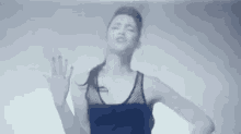 a man in a black tank top is dancing in a dark room with his eyes closed .