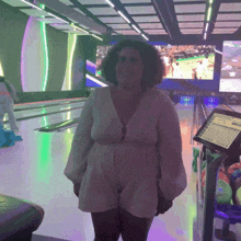 a woman in a white dress stands in front of a bowling alley with a scoreboard in the background
