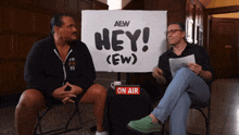 two men are sitting in front of a sign that says hey ( ew )