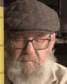 a man with a beard and glasses is wearing a flat cap .
