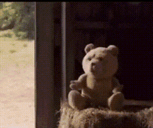 a teddy bear is sitting on a bale of hay in a dark room