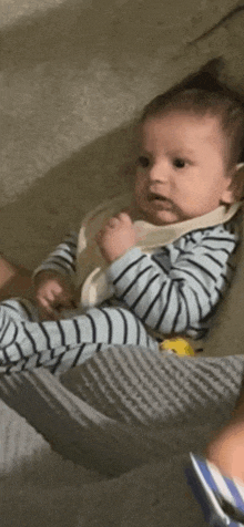 a baby is sitting in a crib wearing a striped shirt .