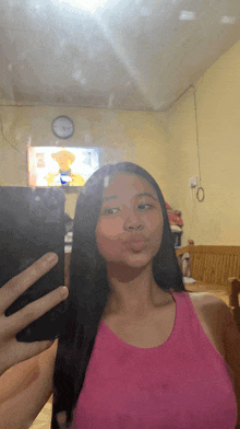 a girl in a pink tank top takes a selfie in front of a clock