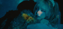 a woman with blonde hair is laying down in a dark room with a blue light behind her