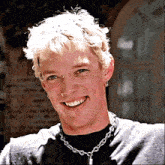 a young man wearing a black shirt and a chain around his neck is smiling