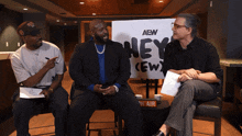 three men sit in front of a sign that says aew hey crew