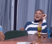 a woman in a striped sweater is sitting at a table with a glass of wine .