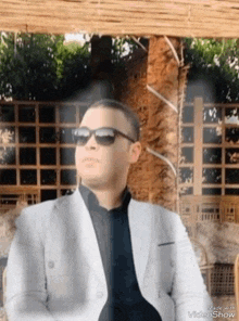 a man wearing sunglasses and a suit is sitting in front of a tree