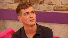 a young man in a black shirt is sitting on a pink couch and looking up .