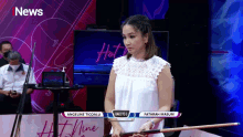 a woman holding a pool cue in front of a tv screen that says i news