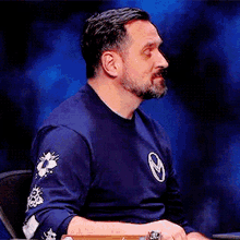 a man with a beard is wearing a blue shirt with a circle on the sleeve