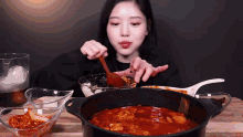 a woman is stirring a pot of sauce with a wooden spoon .