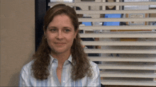 a woman in a blue striped shirt is smiling in front of a window with blinds
