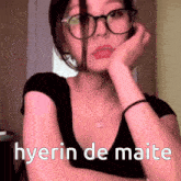 a woman wearing glasses and a black shirt with the words hyerin de maite written on it .