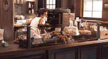 a woman stands behind a counter in a bakery with a sign that says ' bakery ' on it