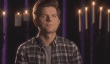 a man in a plaid shirt is standing in front of a wall with candles .