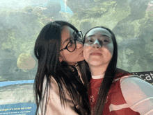 a woman kisses another woman on the cheek in front of a sign that says the length of a moray eel 6 feet