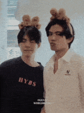 a man wearing a hybs shirt stands next to another man wearing a white shirt