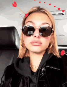 a woman wearing sunglasses and a black jacket has a red arrow in her hair