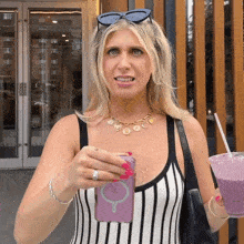 a woman in a striped tank top is holding a purple smoothie and a pink phone