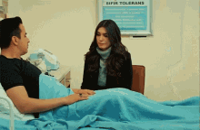a woman sits next to a man in a hospital bed in front of a sign that says safir tolerans