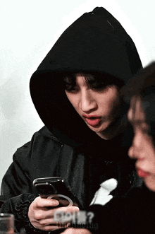 a man in a hooded jacket is looking at his cell phone .