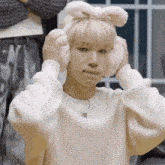 a young man wearing a white sweater and pink ear muffs is making a funny face .