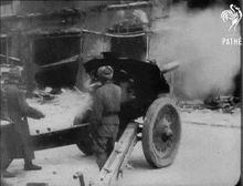 a black and white photo of soldiers shooting a cannon with pathe written on the bottom right